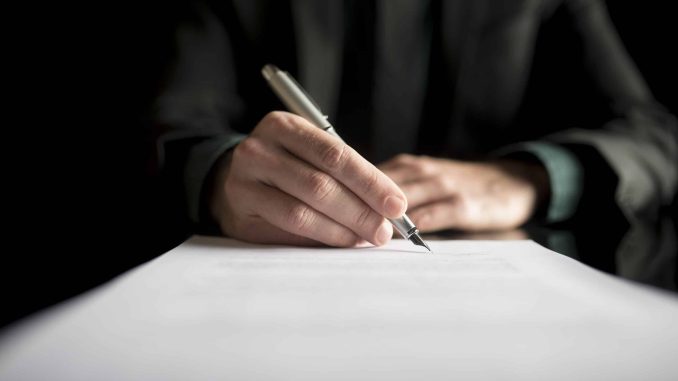 Closeup of lawyer or executive signing a contract, placed on black desk.