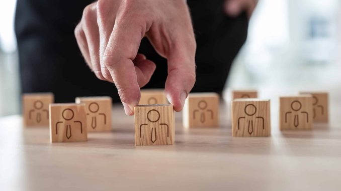 Human resources concept - businessman arranging wooden cubes with people icon on office desk.